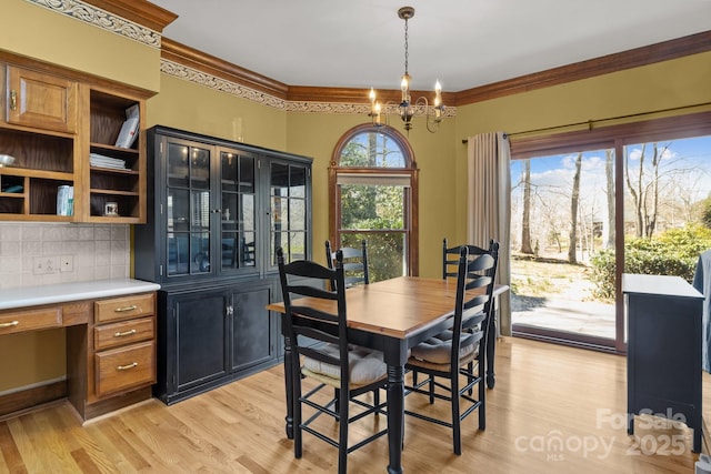 dining space with light wood-type flooring, a chandelier, crown molding, and built in study area