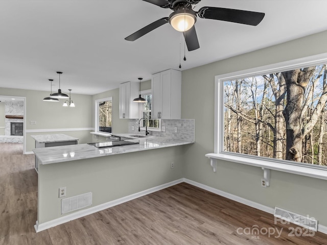 kitchen featuring decorative light fixtures, backsplash, kitchen peninsula, sink, and white cabinets