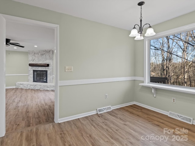 spare room with ceiling fan with notable chandelier, hardwood / wood-style floors, and a fireplace