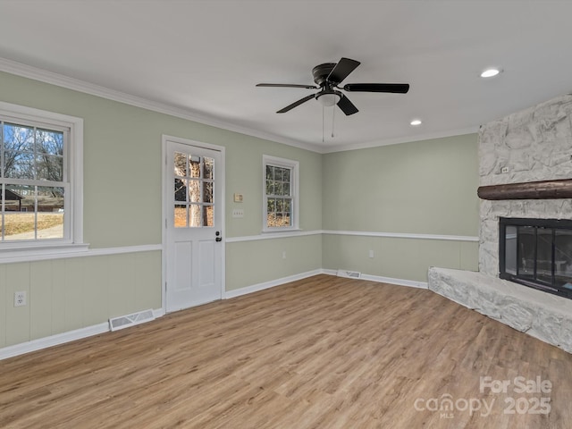 unfurnished living room featuring crown molding, ceiling fan, a stone fireplace, and light hardwood / wood-style floors