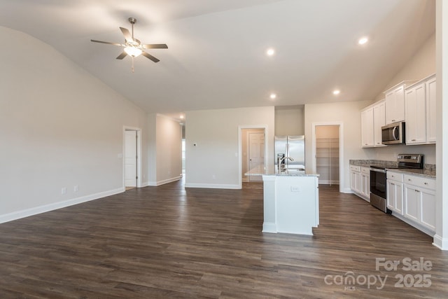 kitchen with vaulted ceiling, light stone countertops, an island with sink, stainless steel appliances, and white cabinets