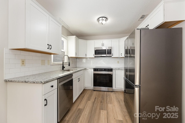 kitchen featuring stainless steel appliances, decorative backsplash, light stone countertops, white cabinets, and sink