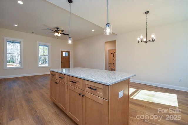 kitchen featuring decorative light fixtures, a center island, light wood-type flooring, light stone countertops, and ceiling fan with notable chandelier