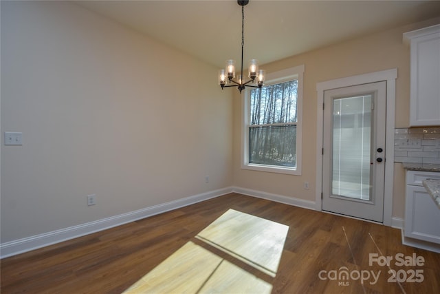 unfurnished dining area featuring a notable chandelier and dark hardwood / wood-style flooring