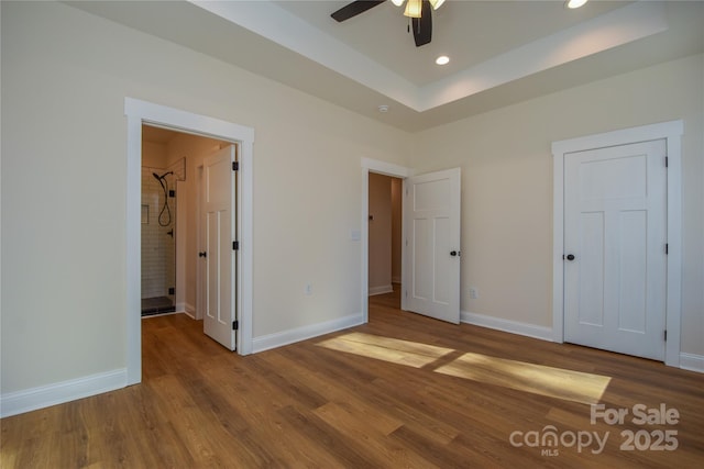 unfurnished bedroom featuring ceiling fan, hardwood / wood-style floors, and a tray ceiling