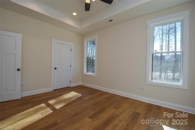 unfurnished bedroom featuring ceiling fan, wood-type flooring, and a raised ceiling