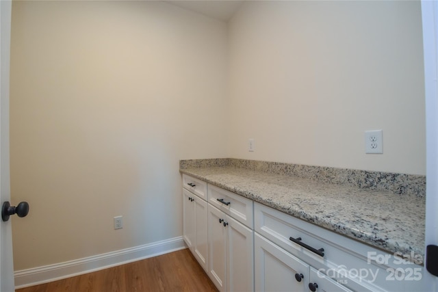 interior space featuring white cabinetry, wood-type flooring, and light stone countertops