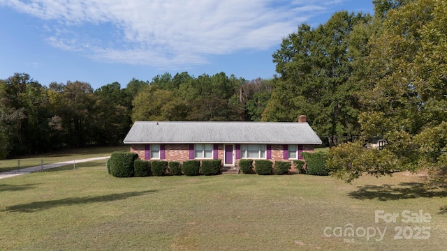 single story home with brick siding, a chimney, a front yard, fence, and a wooded view