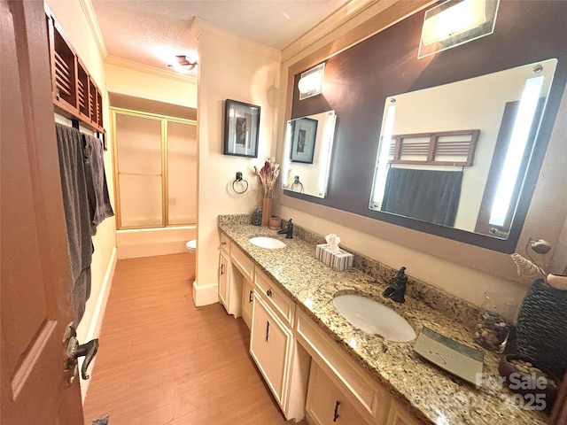 full bathroom featuring combined bath / shower with glass door, wood-type flooring, ornamental molding, vanity, and toilet