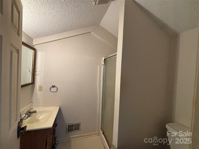 bathroom with vanity, a textured ceiling, vaulted ceiling, a shower with shower door, and toilet