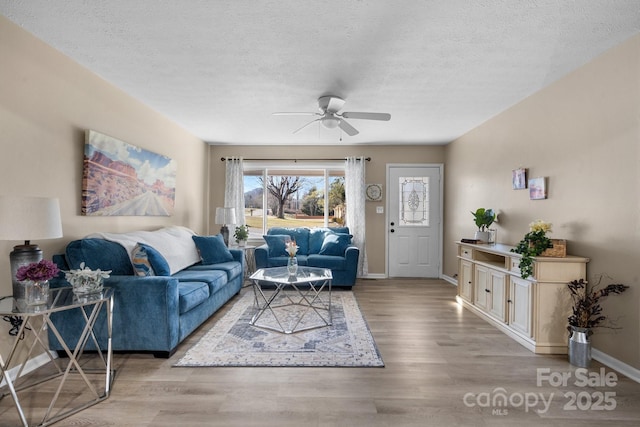 living room with a textured ceiling, ceiling fan, and light wood-type flooring