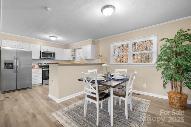 dining room featuring light wood-type flooring, ornamental molding, and a textured ceiling