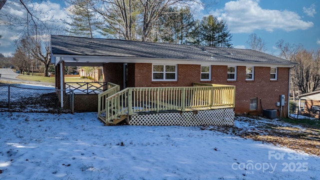 snow covered back of property with a deck and central AC unit