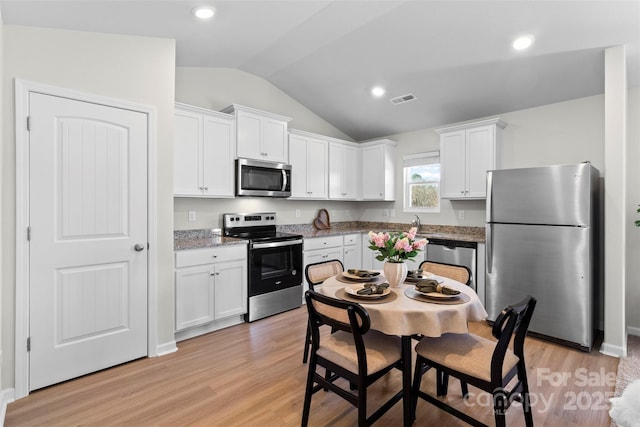 kitchen with white cabinets, appliances with stainless steel finishes, light wood-type flooring, vaulted ceiling, and light stone counters