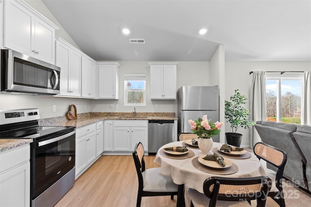 kitchen featuring light stone countertops, white cabinets, appliances with stainless steel finishes, sink, and light hardwood / wood-style flooring