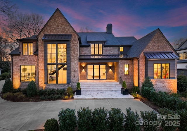 back of property at dusk featuring metal roof, brick siding, a standing seam roof, and a chimney