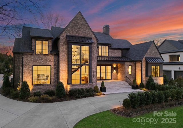 view of front of property featuring metal roof, brick siding, driveway, a standing seam roof, and a chimney