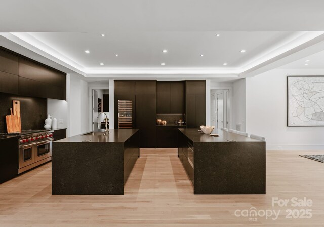 kitchen featuring dark countertops, a raised ceiling, a center island with sink, and a sink