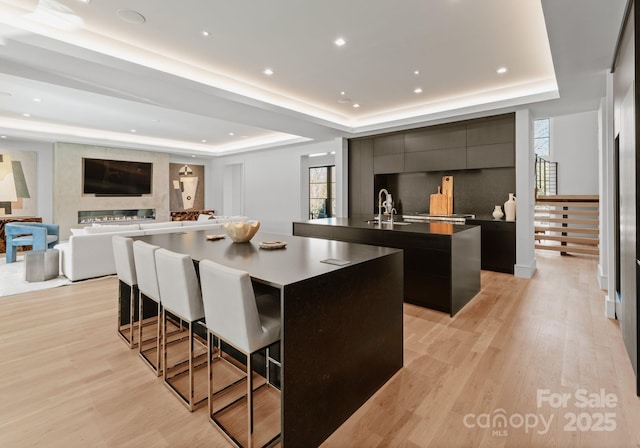 kitchen featuring a raised ceiling, modern cabinets, a breakfast bar area, open floor plan, and a large island with sink