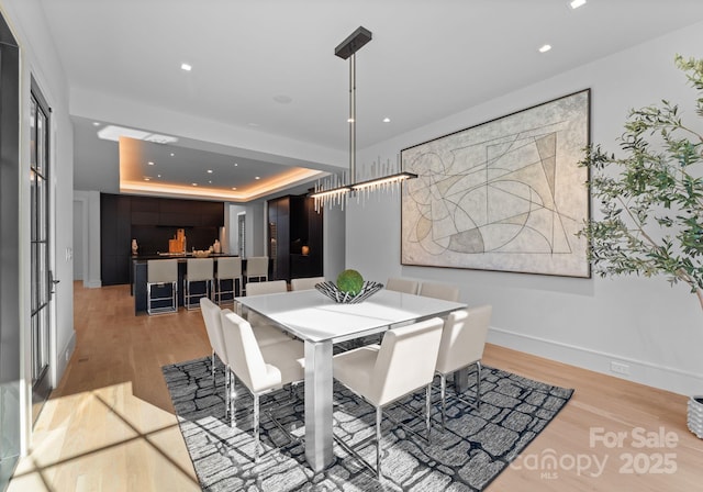 dining space featuring light wood-style floors, a tray ceiling, baseboards, and recessed lighting