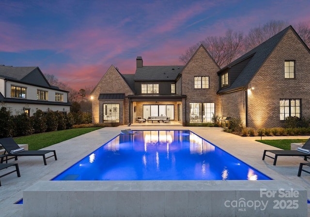 pool at dusk featuring an outdoor pool and a patio