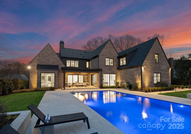 pool at dusk featuring a yard, an outdoor pool, and a patio