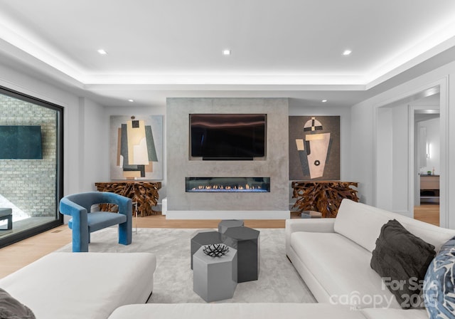 living area with light wood-style flooring, a fireplace, a raised ceiling, and recessed lighting