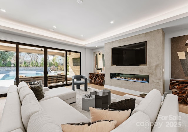 living room featuring recessed lighting, wood finished floors, a tray ceiling, and a premium fireplace