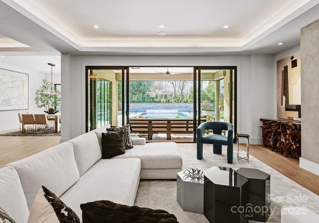 living room with baseboards, a raised ceiling, and light wood-style floors