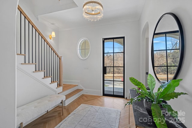 entryway with ornamental molding, a healthy amount of sunlight, a chandelier, and light parquet flooring