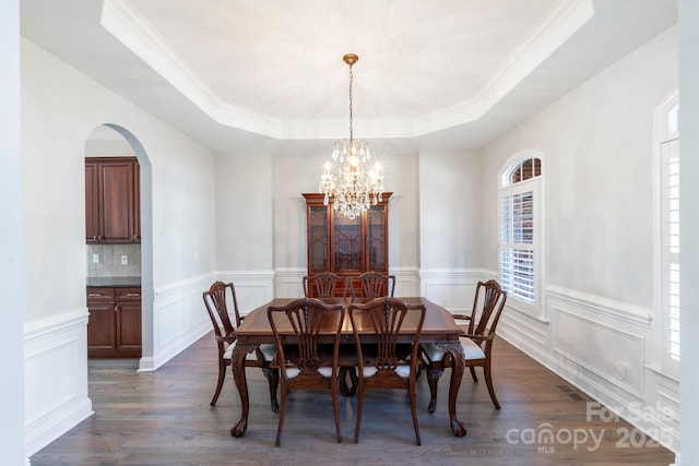 dining room featuring crown molding, dark hardwood / wood-style flooring, a raised ceiling, and a notable chandelier