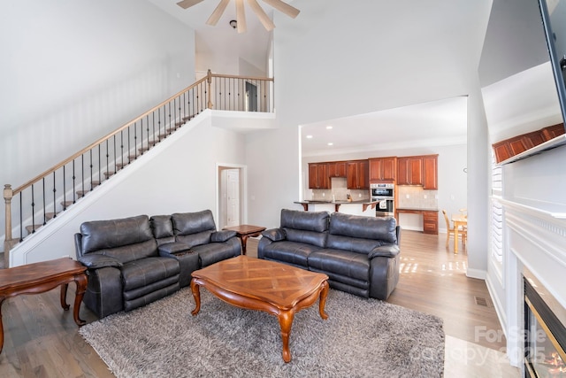 living room with ceiling fan, light hardwood / wood-style flooring, and a towering ceiling