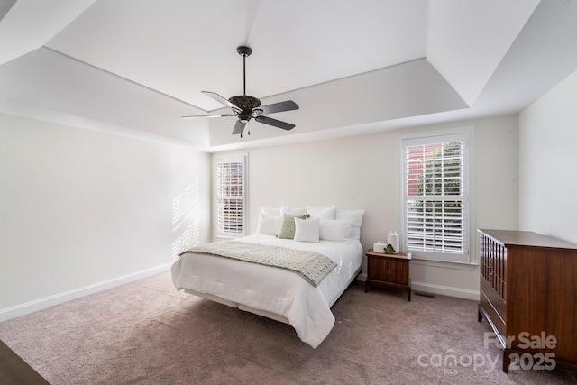 carpeted bedroom with ceiling fan and a raised ceiling