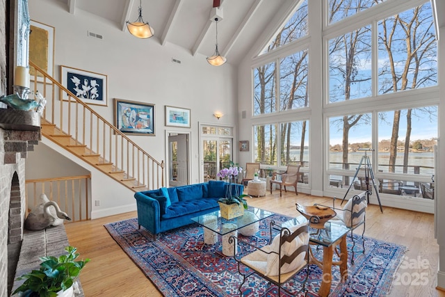 living room featuring a brick fireplace, light hardwood / wood-style flooring, beam ceiling, and a towering ceiling