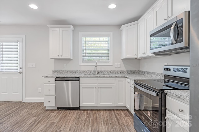 kitchen with light hardwood / wood-style floors, sink, white cabinetry, stainless steel appliances, and light stone counters