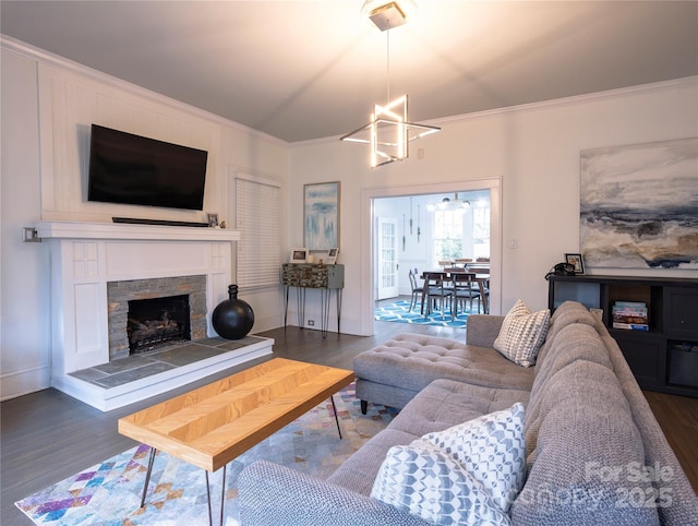 living room featuring dark hardwood / wood-style flooring, a stone fireplace, ornamental molding, and a chandelier