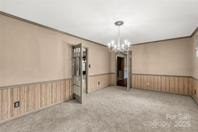 carpeted spare room featuring crown molding, a chandelier, and wood walls