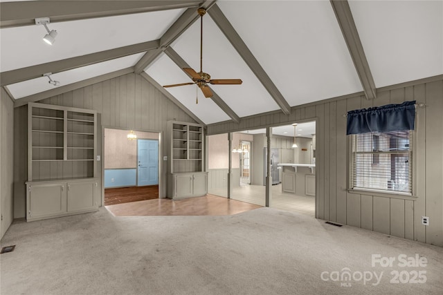 unfurnished living room with ceiling fan, wooden walls, light colored carpet, and beam ceiling