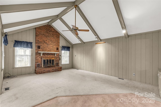 unfurnished living room with a brick fireplace, vaulted ceiling with beams, a healthy amount of sunlight, and carpet flooring