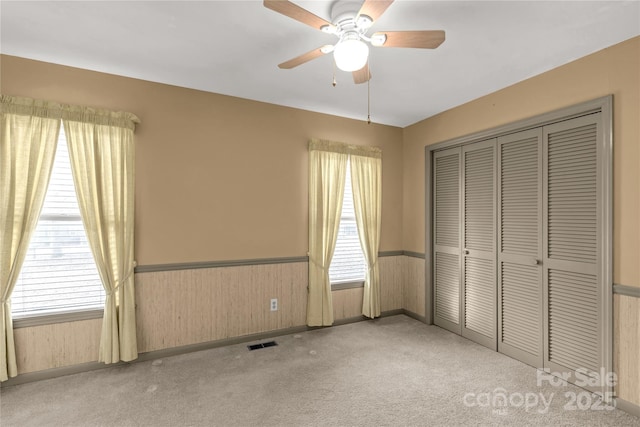 unfurnished bedroom featuring multiple windows, light carpet, ceiling fan, and a closet