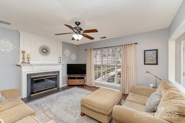 living room with hardwood / wood-style floors, a large fireplace, a textured ceiling, and ceiling fan