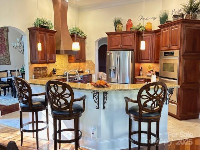 kitchen featuring light stone countertops, wall chimney exhaust hood, decorative light fixtures, stainless steel fridge, and light tile patterned flooring