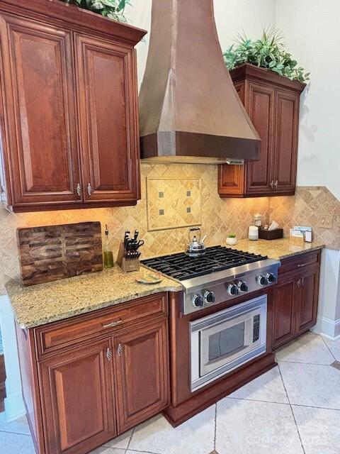 kitchen featuring stainless steel gas cooktop, wall chimney exhaust hood, light tile patterned floors, and light stone counters