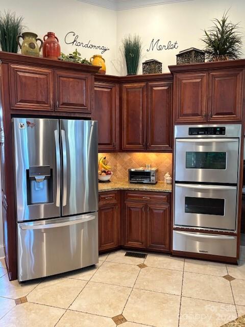 kitchen featuring tasteful backsplash, light tile patterned floors, light stone counters, and stainless steel appliances