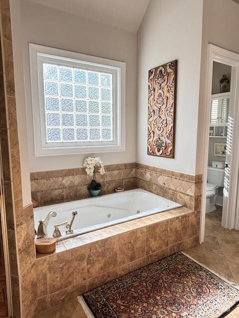 bathroom featuring lofted ceiling, tile patterned flooring, toilet, and a relaxing tiled tub