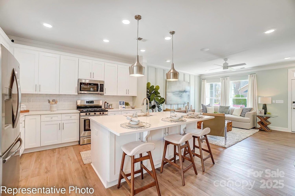 kitchen with white cabinetry, ceiling fan, appliances with stainless steel finishes, a kitchen island with sink, and decorative light fixtures