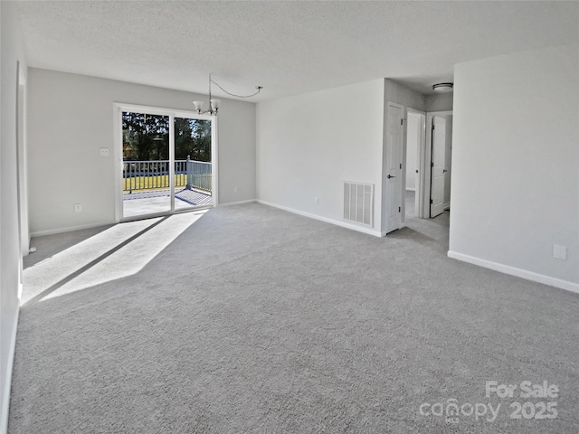 carpeted spare room featuring a textured ceiling and a chandelier