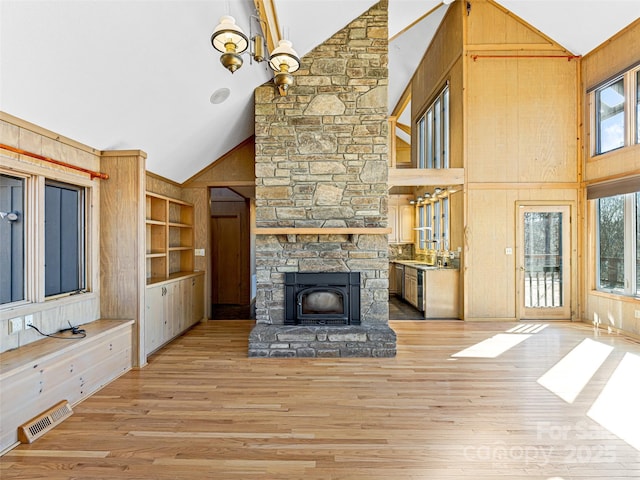 unfurnished living room featuring a stone fireplace, built in features, high vaulted ceiling, wood walls, and light hardwood / wood-style floors