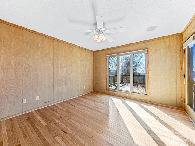 unfurnished room featuring ceiling fan, light wood-type flooring, a textured ceiling, and wood walls