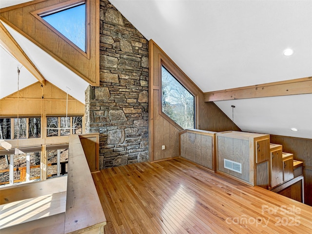 bonus room featuring vaulted ceiling with beams, wooden walls, and light wood-type flooring